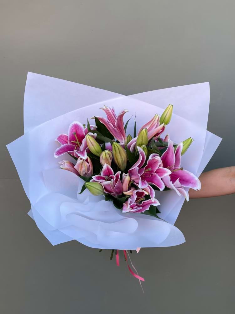 Bouquet of white or pink oriental lilies wrapped in white paper, partially closed buds ready to bloom