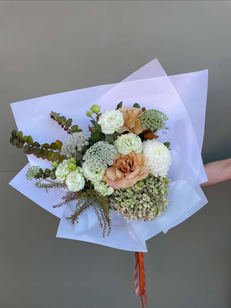 Neutral toned bouquet with hydrangea, roses and soft green foliage wrapped in white paper
