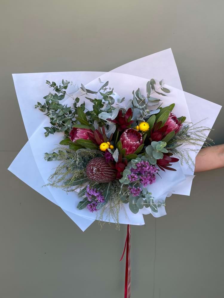 Dark toned bouquet with native flowers, berries and greenery wrapped in white paper.